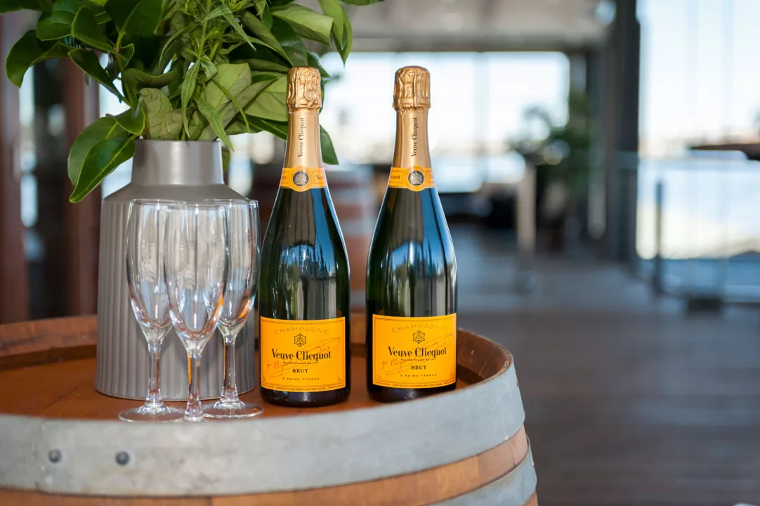 Empty champagne flutes next to two bottles of Veuve Cliquot on a wine barrel