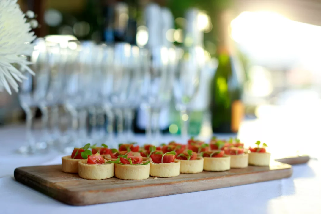 Mini quiches served on a wooden board with empty champagne glasses in the background