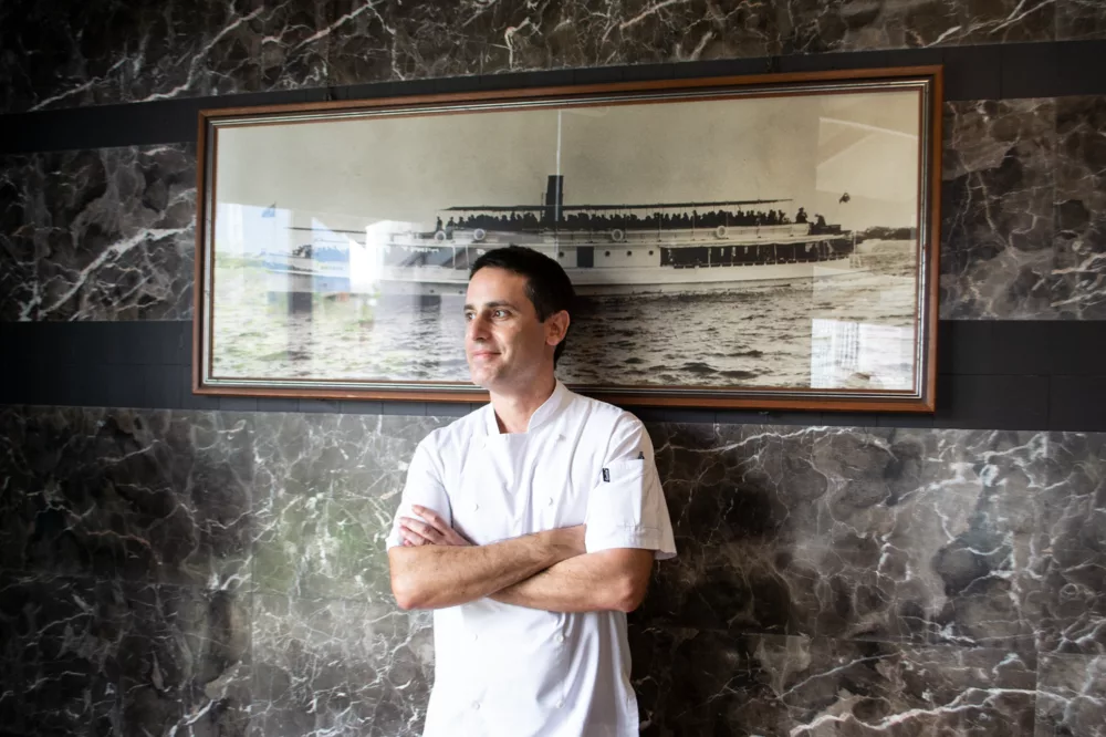 Head chef stands against a wall with a photo of a boat