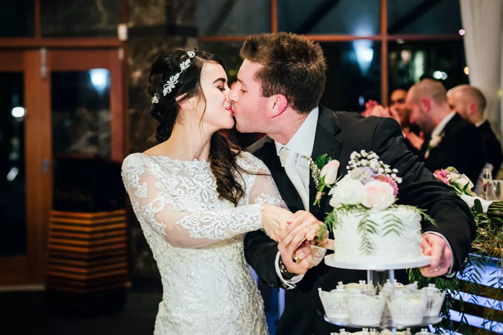 A bride and groom kiss as they cut the wedding cake