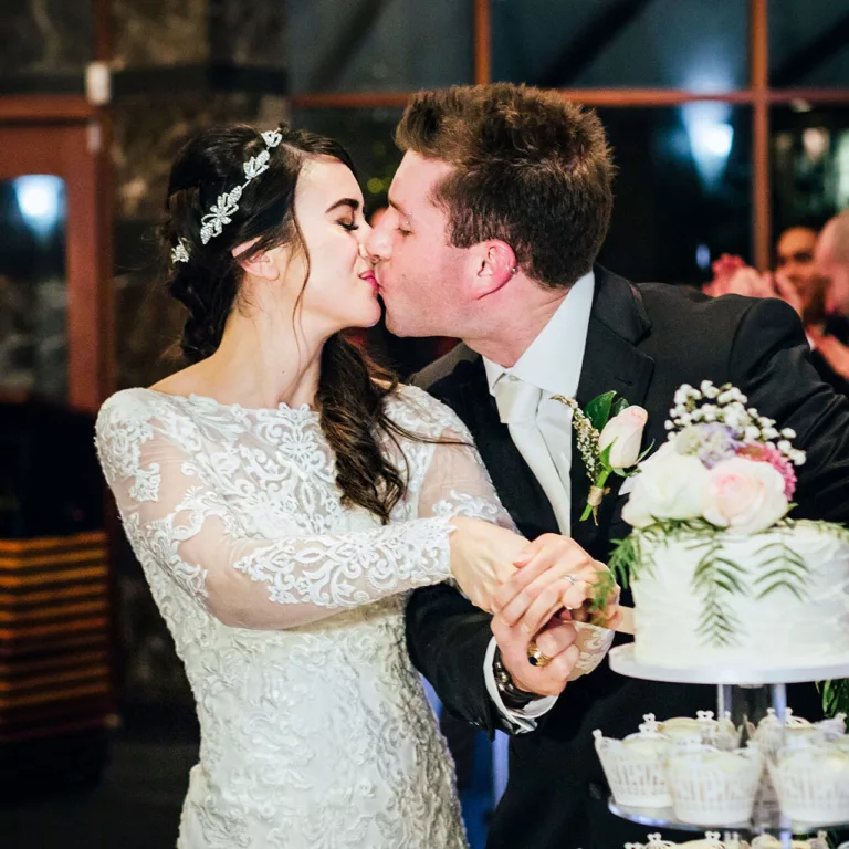 A bride and groom kiss as they cut the wedding cake