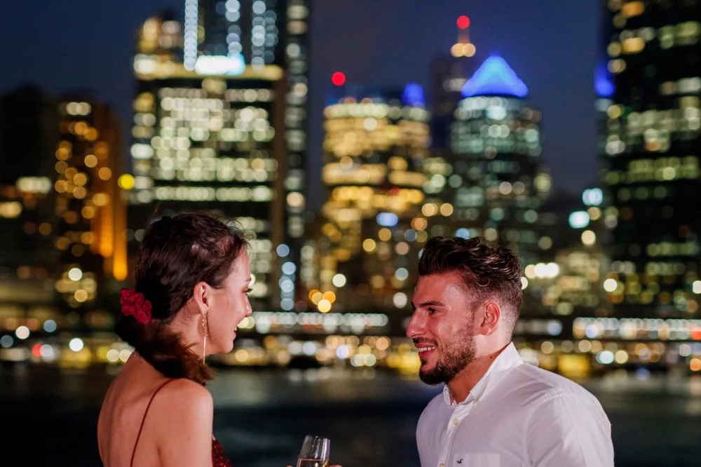 Smart casual premium couple having wine on open deck night time dinner with city lights in the background