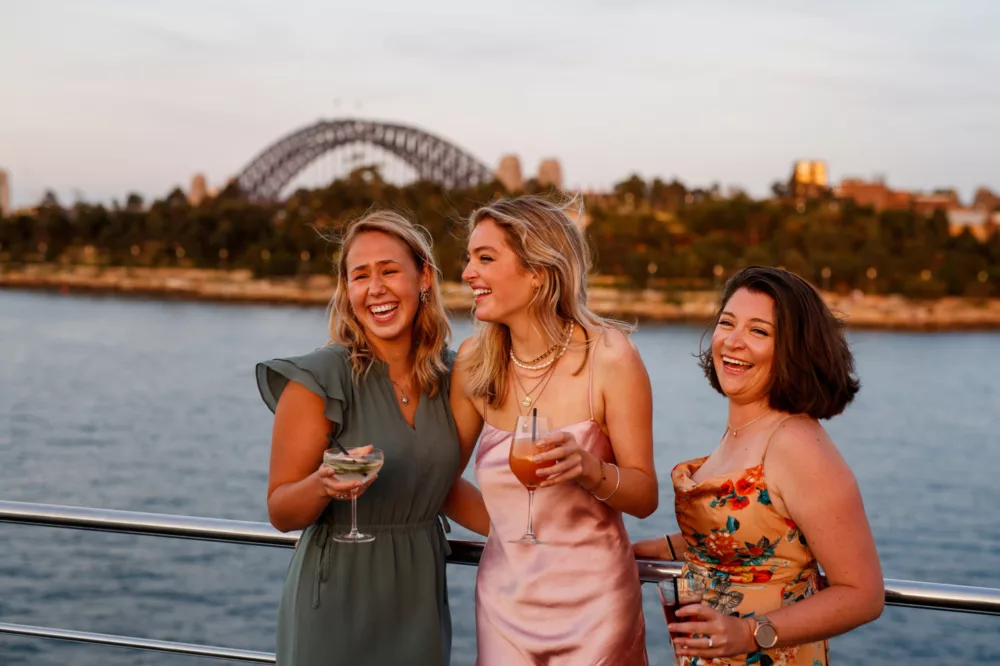 Group of girls laughing and having drinks on the open deck with Barangaroo and Harbour Bridge in the background