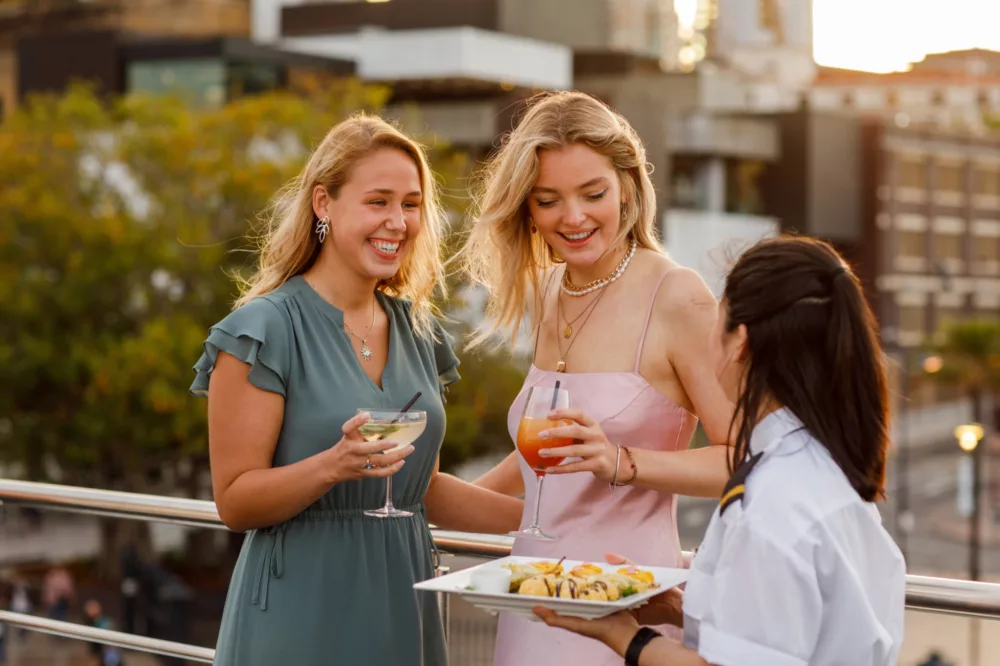 Girls having cocktails and eating canapés on the open deck with city in the background