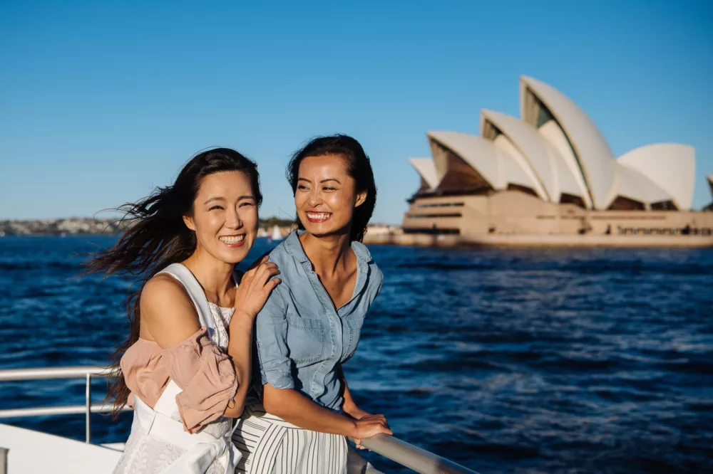 Two girlfriends cheering and enjoying the view of the Sydney Opera House sightseeing ferry non-ccc dnsw