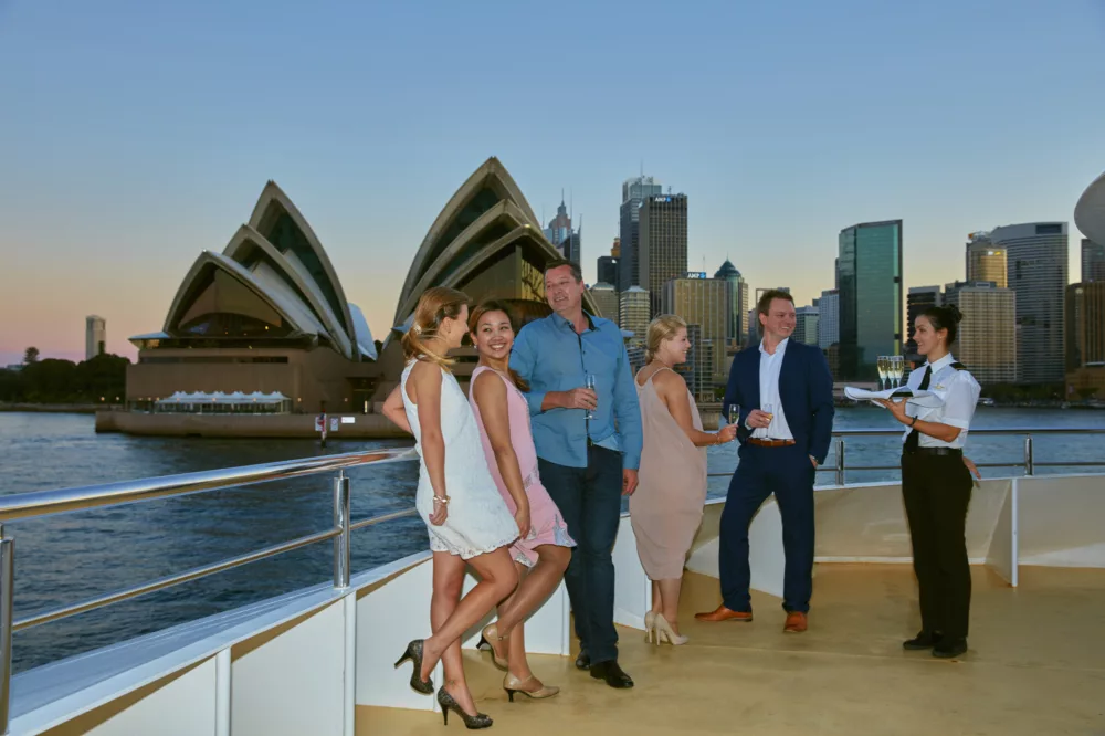 Group having Cocktails outside Sirius Room of Sydney 2000 boat with crew serving at Sunset charter fleet