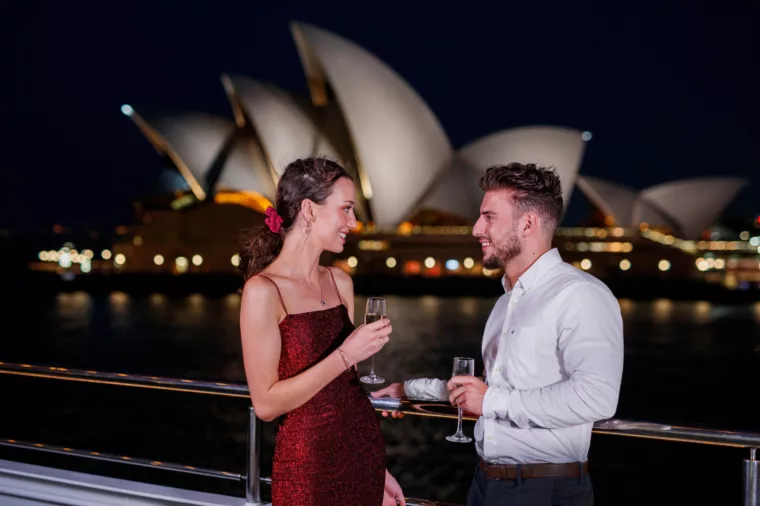 Young couple having drinks celebrating anniversary Gold Penfolds champagne night time Opera House