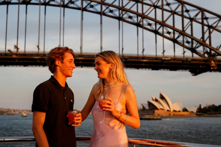 Young couple having cocktail drinks during sunset with Harbour Bar and Opera House in the background