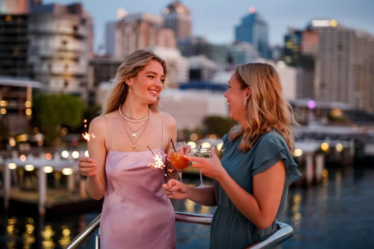 Two girls celebrating with cocktail drinks outdoors with Darling Harbour in the background