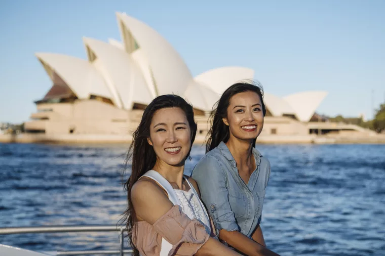 Two asian girls friends on ferry sightseeing HOHO with Opera House in the background