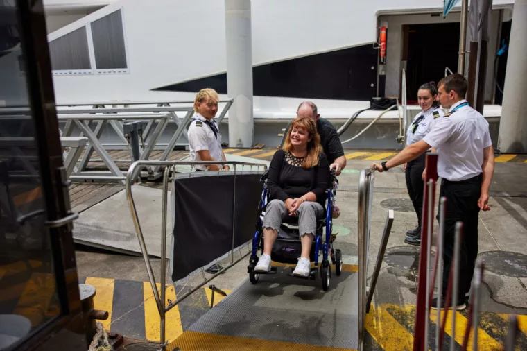 Couple boarding boat with wheelchair as crew supervise