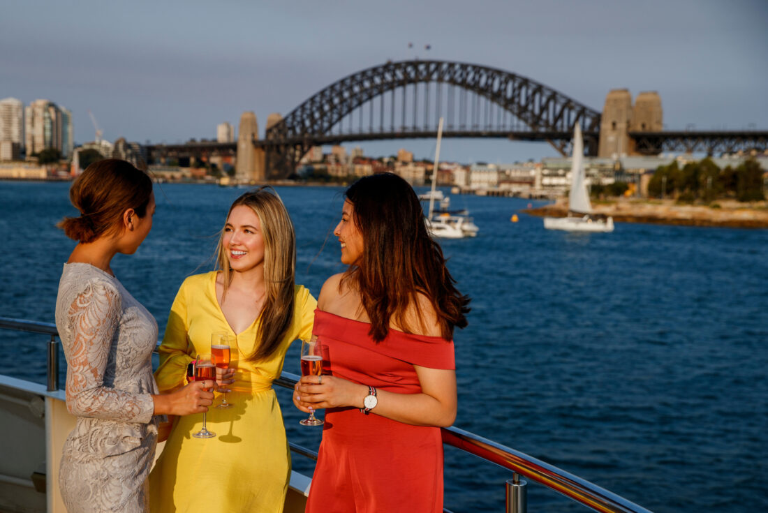 Group of girls enjoying pink champagne on the open deck with Harbour Bridge and Barangaroo in the background, christmas party