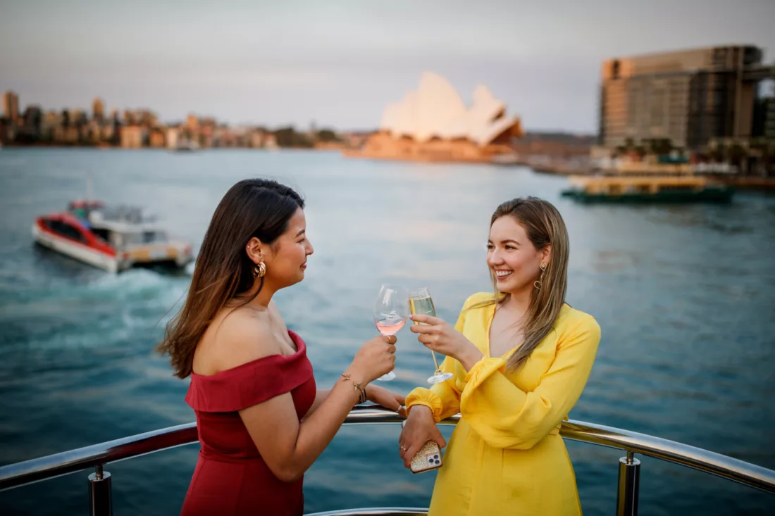 Two girls toasting champagne flute with Opera House and Rocket ferry in the background