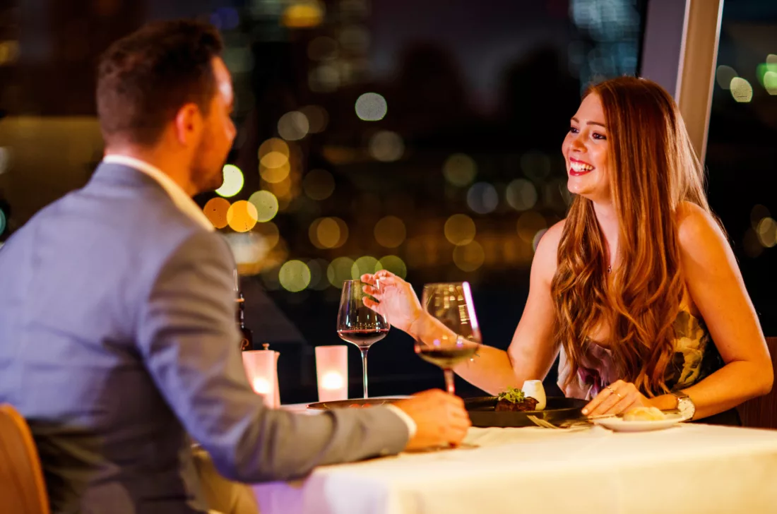 Premium couple having Brilliant Dinner with red wine glass and city lights in the background
