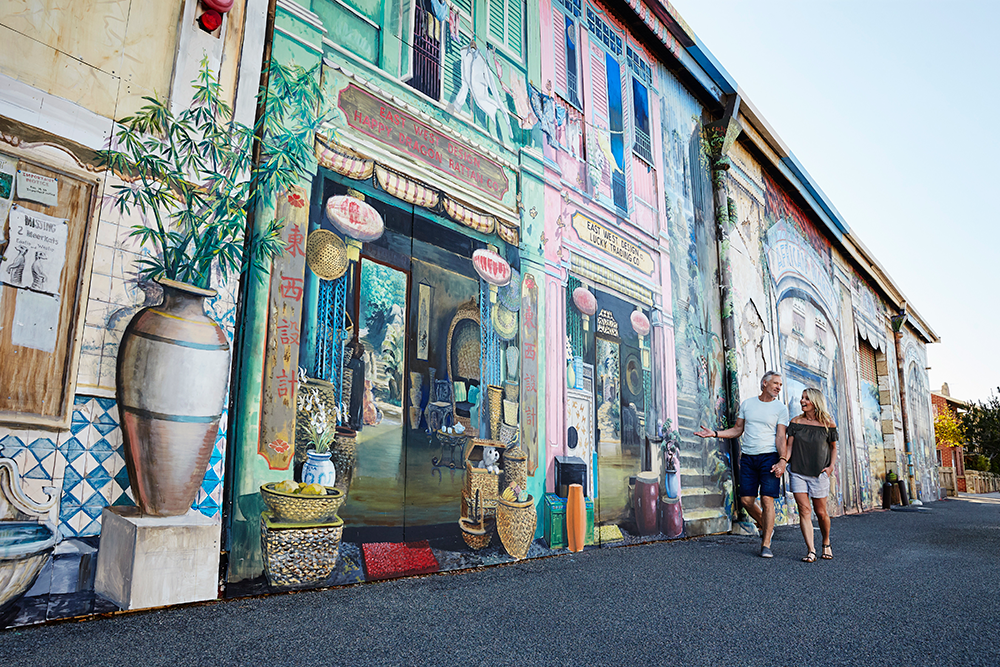 Couple walks past the East West mural