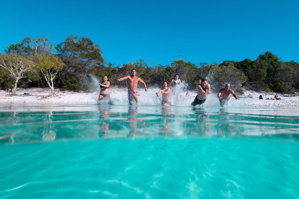 A group runs into the crystal-clear water of Lake McKenzie on K'gari Fraser Island.