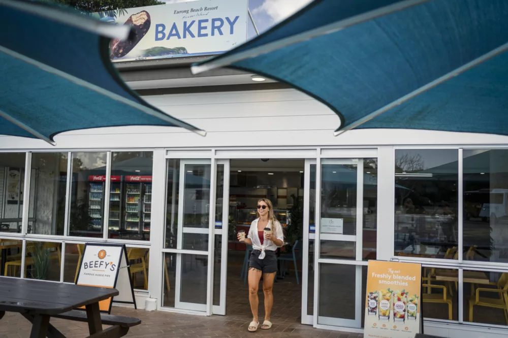 Girl walking out of Eurong Bakery with coffee, K'gari Beach Resort, K'gari (Fraser Island)