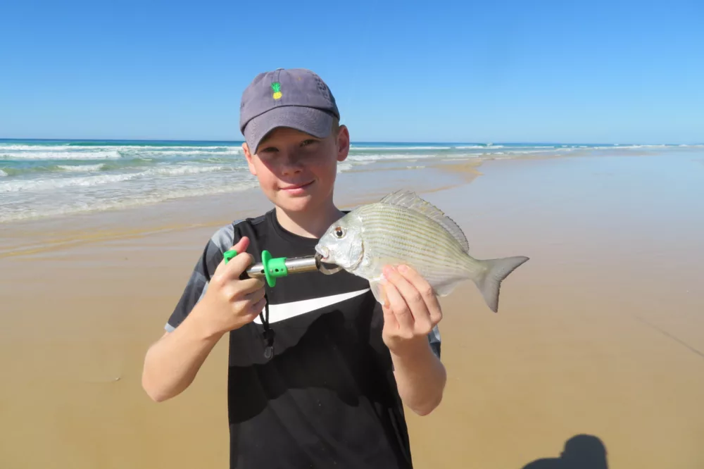 Kid holding fish on beach, K'gari (Fraser Island)