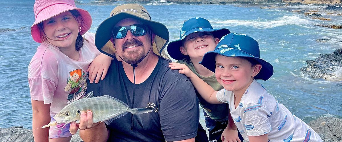 Brett with kids holding a silver trevally caught from the rocks near Snelling Beach