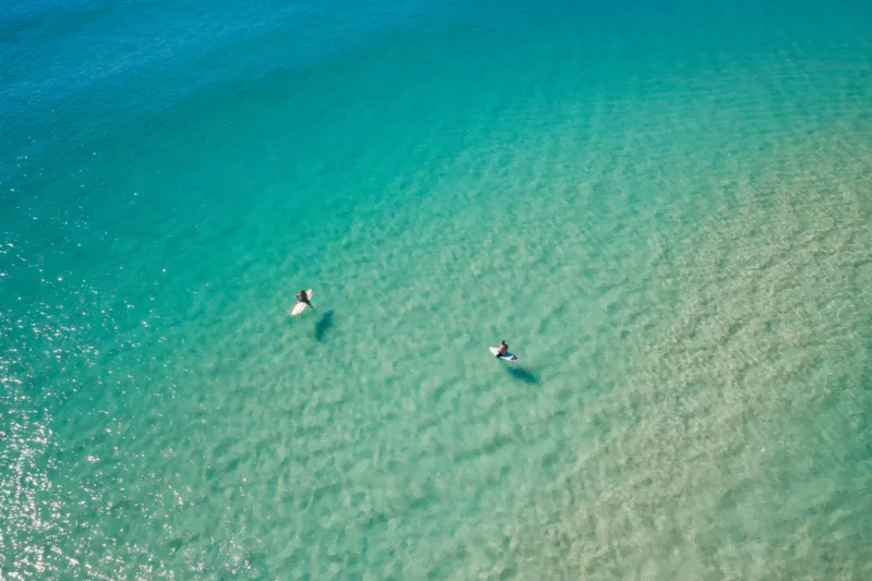 An aerial shot of two surfers on crystal clear blue water