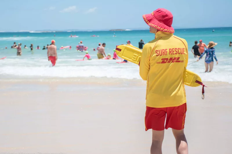Lifesaver on beach holding rescue tube, watching swimmers