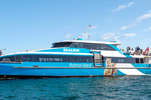 A blue ferry sails in the water as a jetty is seen in the background at Rottnest Island