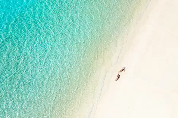Aerial view of Whitehaven Beach with two women relaxing on white silica sand beside the turquoise shoreline.
