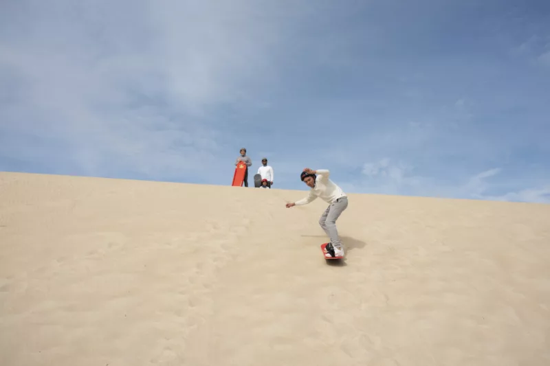 Family having fun tobogganing and sandboarding in Little Sahara