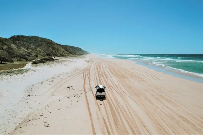 4WD vehicle drives up a golden sandy beach with clear blue skies.