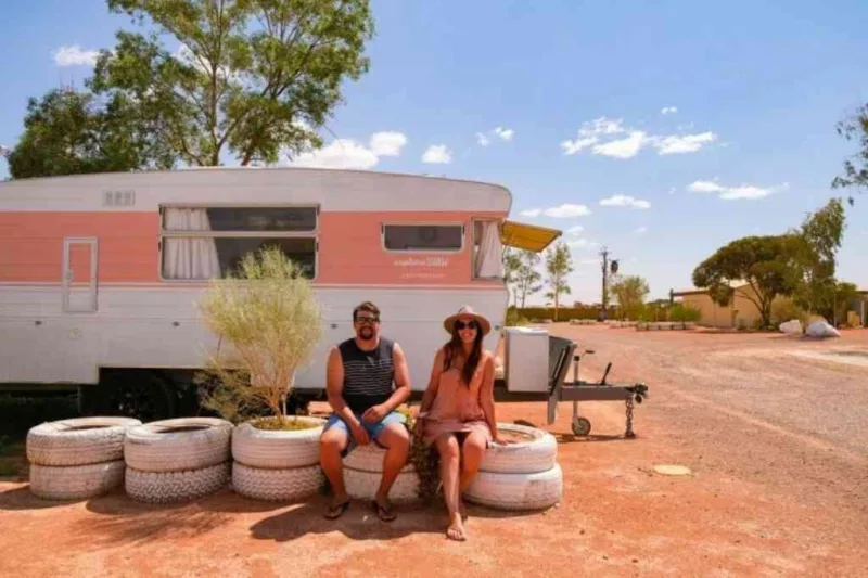 A man and a woman sit on tyres outside their camper van home