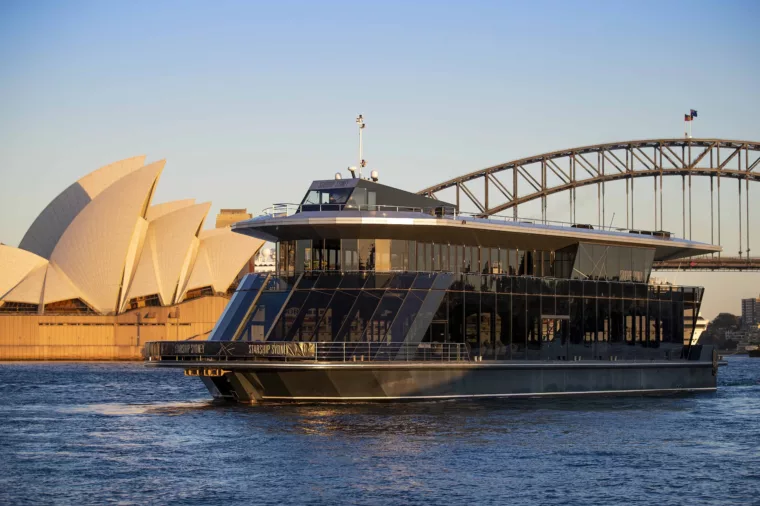 Starship Sydney cruising past the Sydney Opera House and Harbour Bridge at golden hour